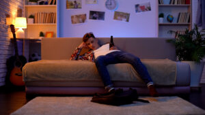 A teenage boy drinking at home on the couch.