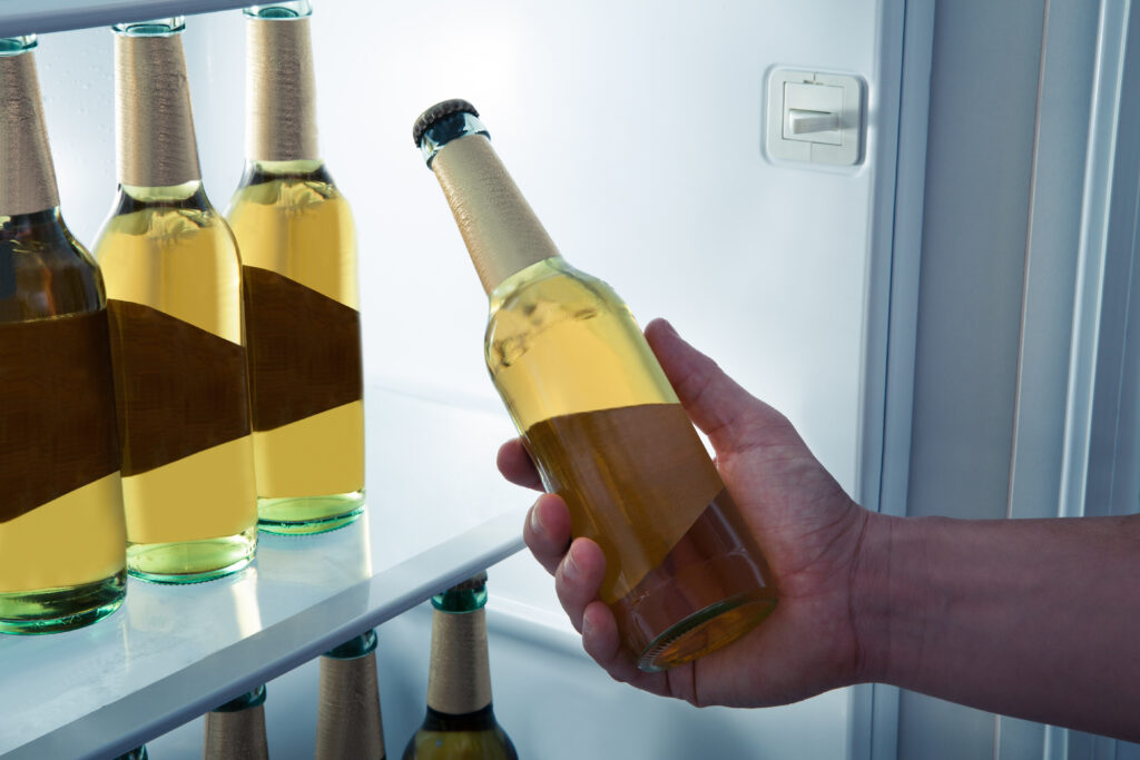 A teenager taking a bottle of beer out of a refrigerator.