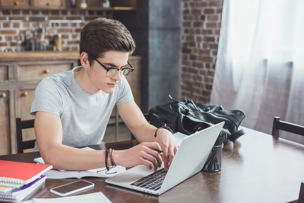 Male,Student,Doing,Homework,And,Typing,On,Laptop,At,Home