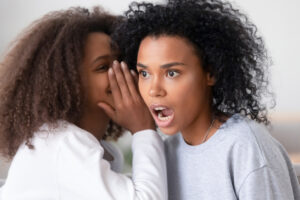 teen daughter whispering in ear of shocked young mother telling secret rumors or unbelievable news, surprised black mom sister friend and teenager girl talking gossiping at home