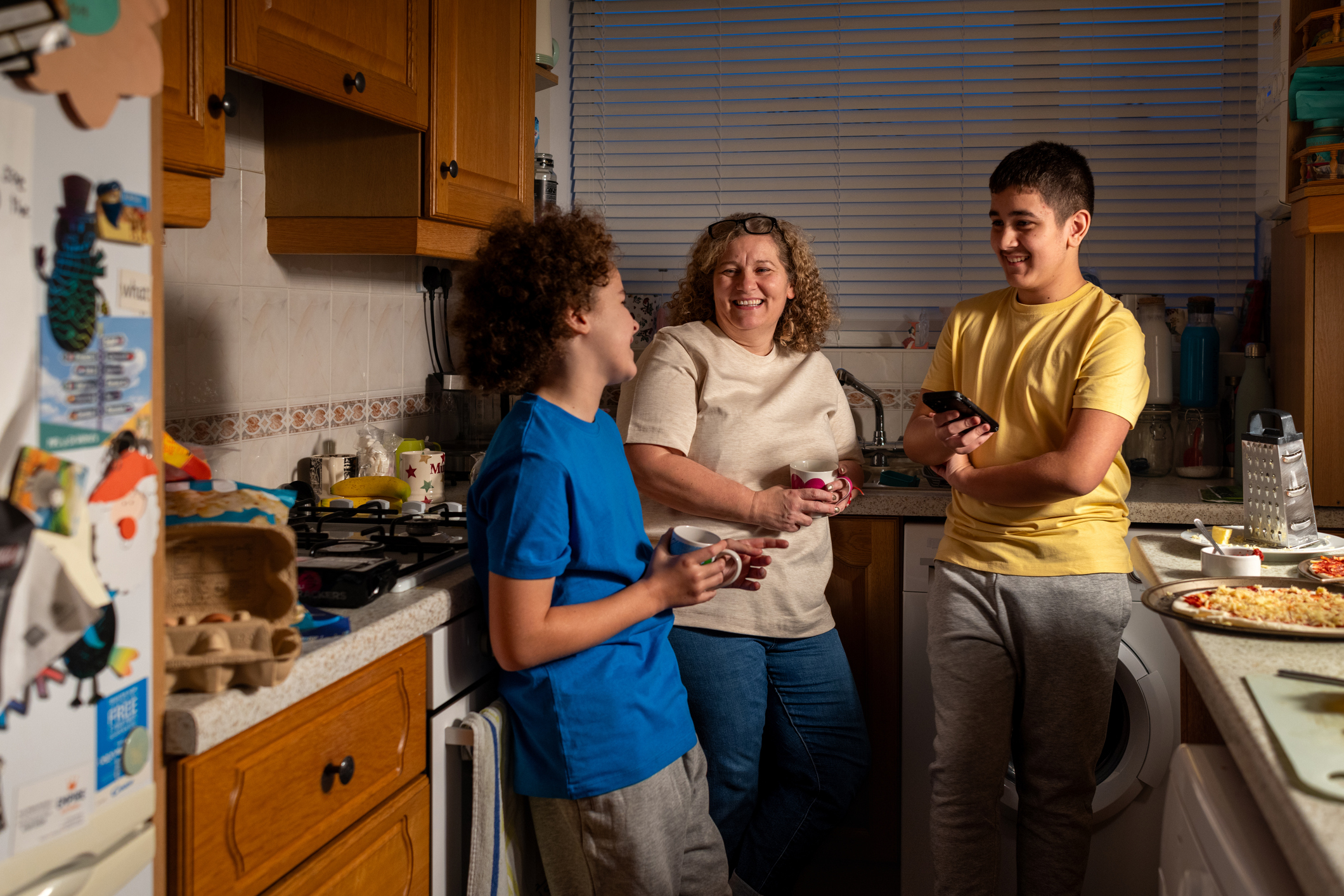 A three-quarter length shot of a cheerful family moment in the kitchen featuring a mother and her two teenage children.