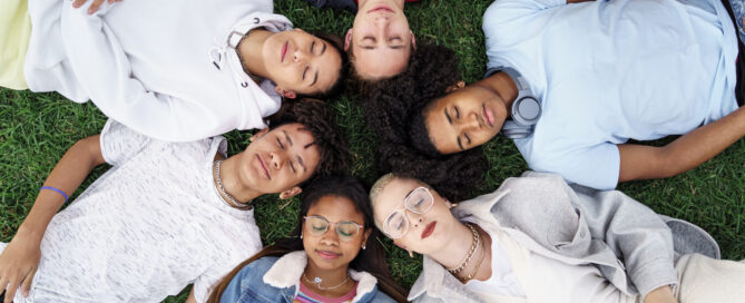 Relaxed teenager friends lying together on green grass with eyes closed, dreaming and sleeping
