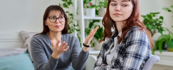 Conflict between mother and teen daughter, offended teenage girl sitting with back to upset arguing mother, on couch at home. Family, difficulties, problems, differences between two generations
