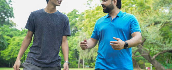 Father and son talking while walking in a public summer park or garden. bonding, parenthood concept.