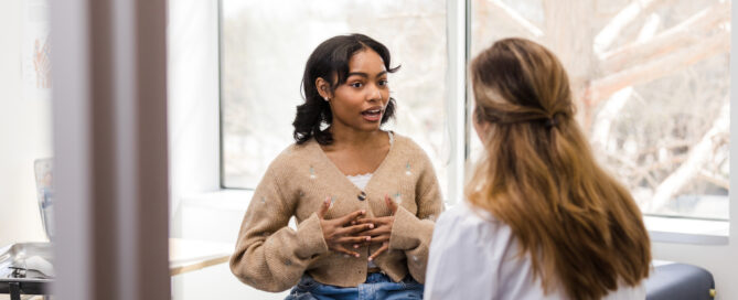 Young adult female patient gestures while explaining her mental health struggles with the doctor
