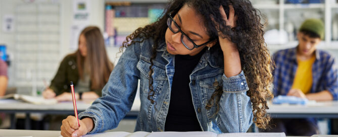Tired female student writing in class during exam.
