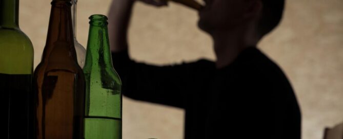 Silhouette of a young male drinking from a bottle with empty ones in the forground