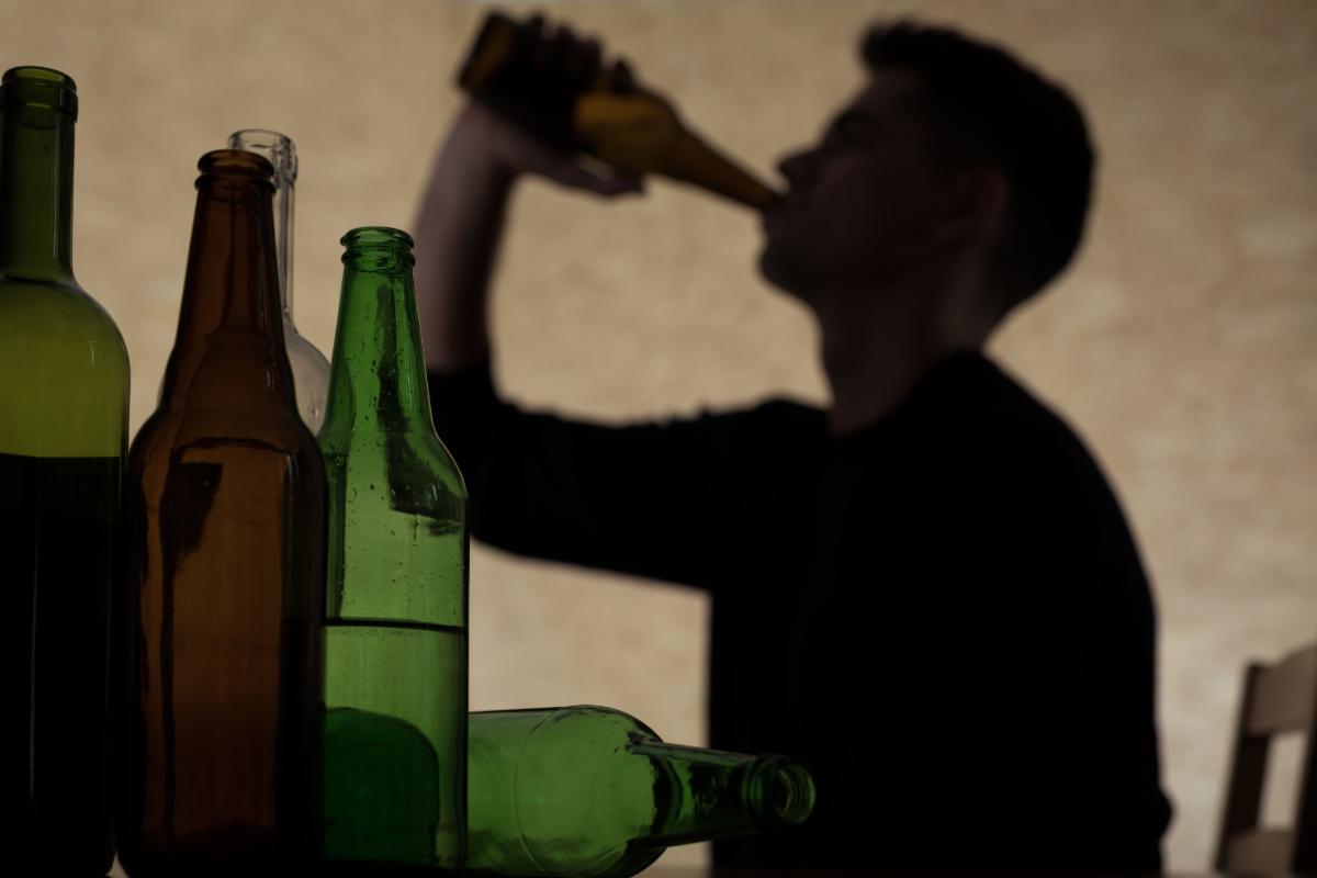 Silhouette of a young male drinking from a bottle with empty ones in the forground